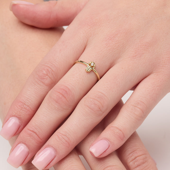 Gold ring with a small diamond on a hand with pink nail polish.