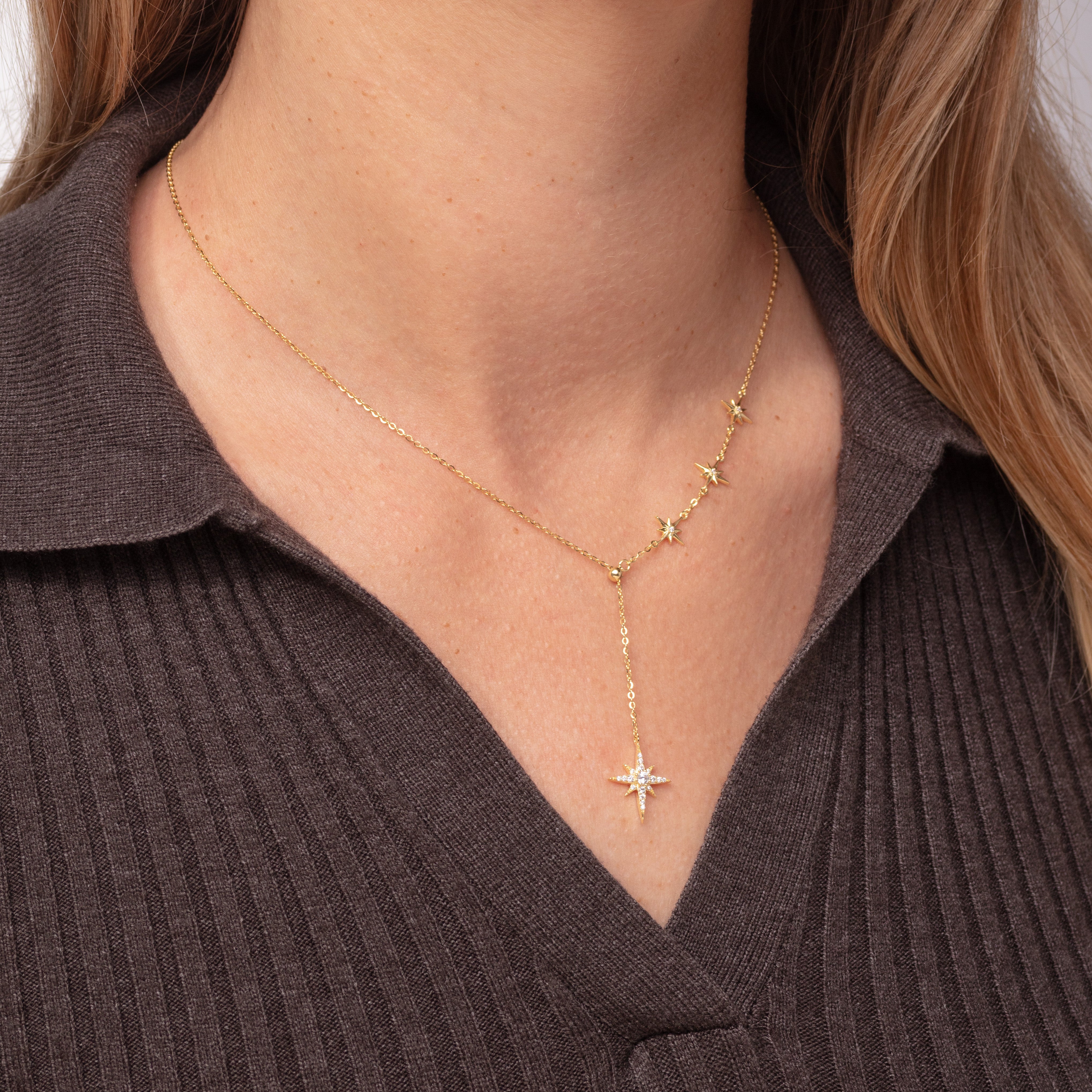 Gold necklace with star pendants worn by a person in a brown ribbed sweater.