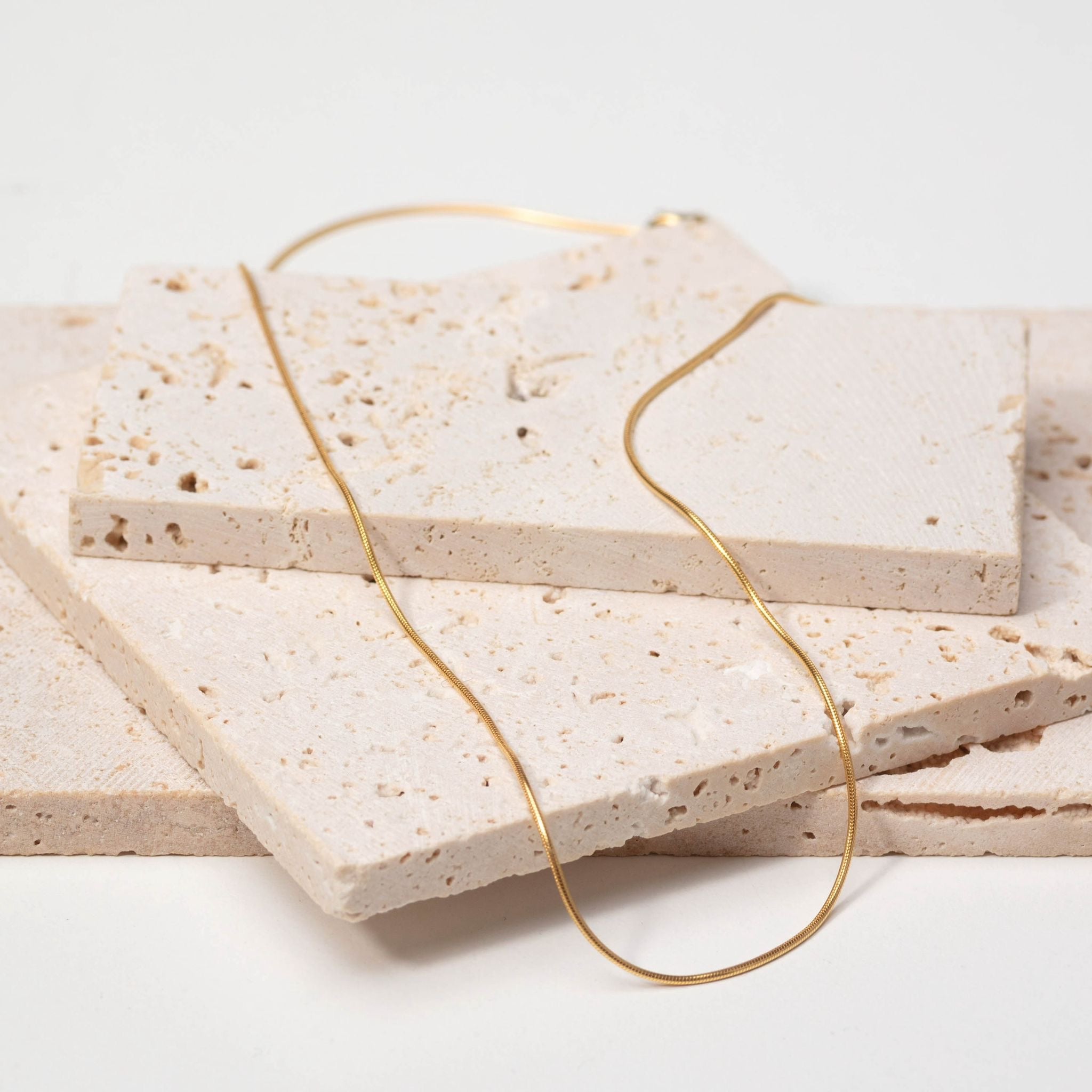 Gold necklace on a stack of beige stone tiles