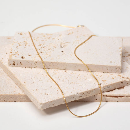 Gold necklace on a stack of beige stone tiles