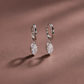 A pair of silver hoop earrings with marquise-cut clear gemstones, displayed on a textured dusty rose surface with soft shadows.