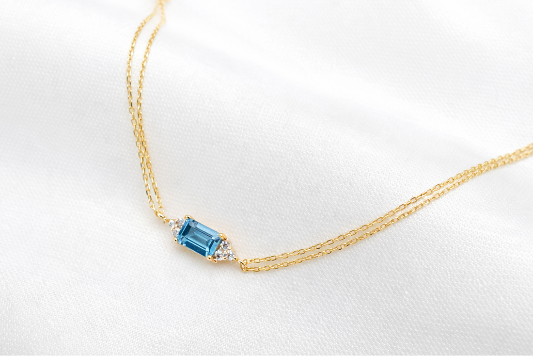 Gold necklace with a blue gemstone on a white background