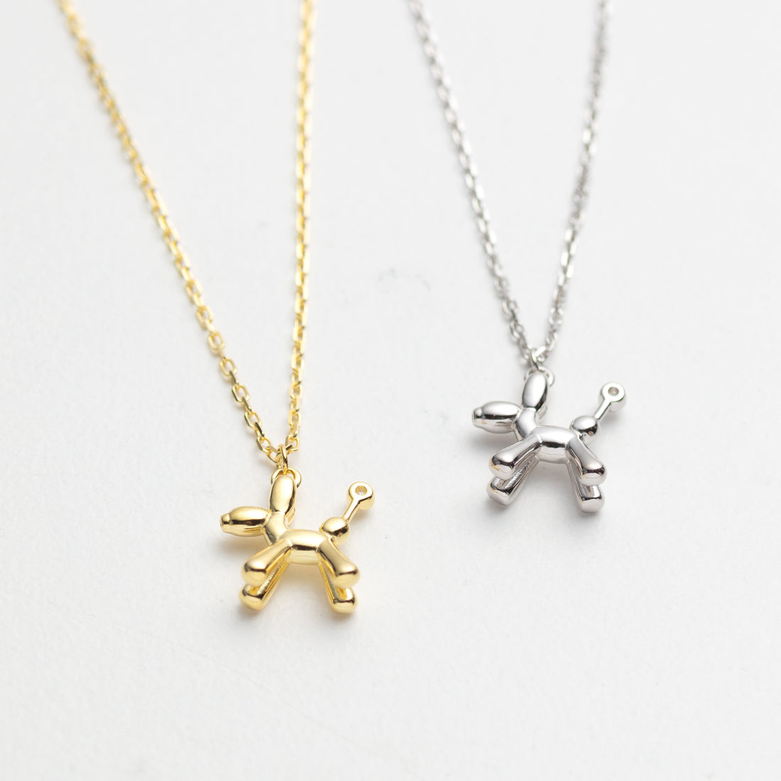 Gold and silver balloon dog pendants on white backgrounds