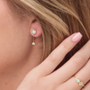 Close-up of a person wearing gold earrings with gemstones and a matching ring.