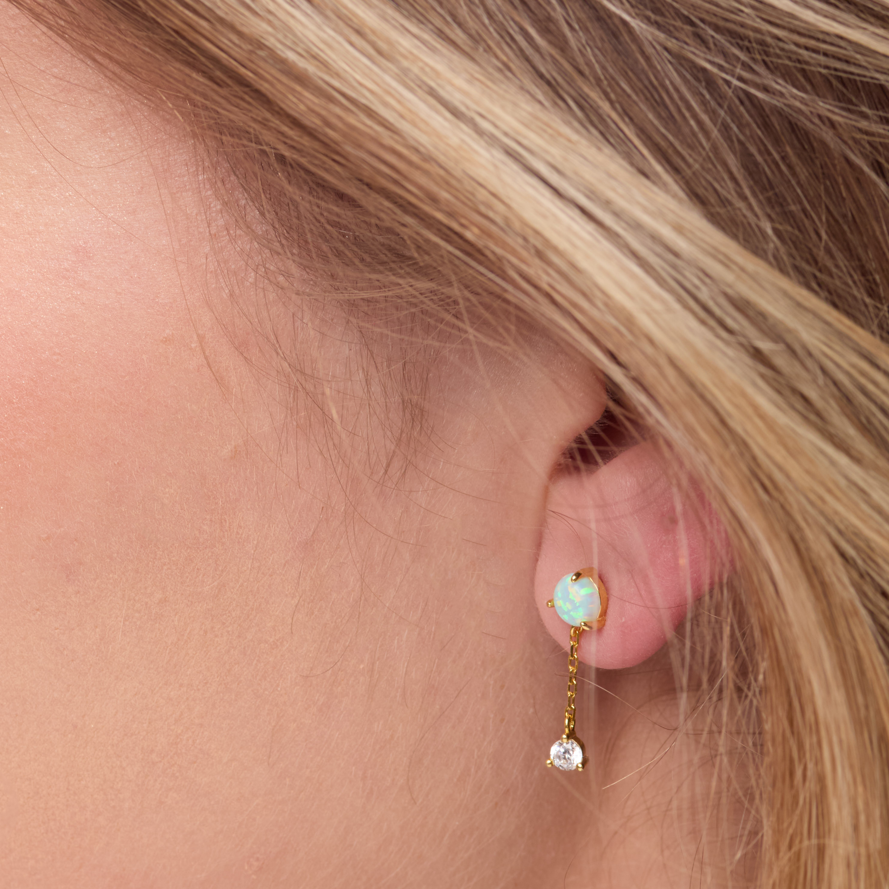 Close-up of an ear wearing a gold earring with a gemstone and a small chain.