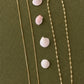 Two gold necklaces on a green surface with small white shells.