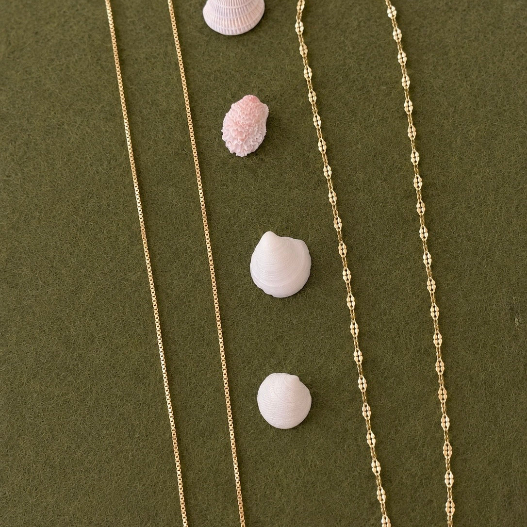 Two gold necklaces on a green surface with small white shells.
