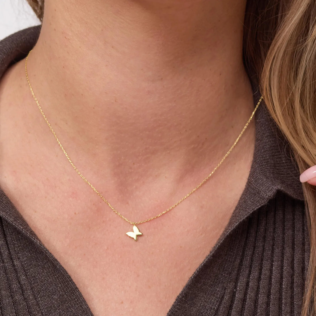 Gold necklace with a butterfly pendant worn by a person