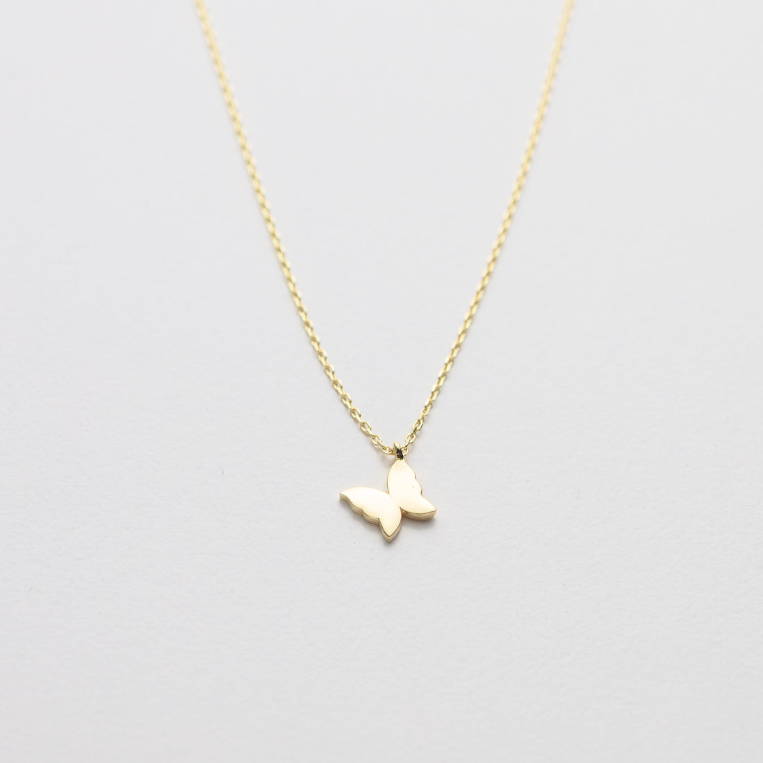 Gold butterfly necklace on a light gray background