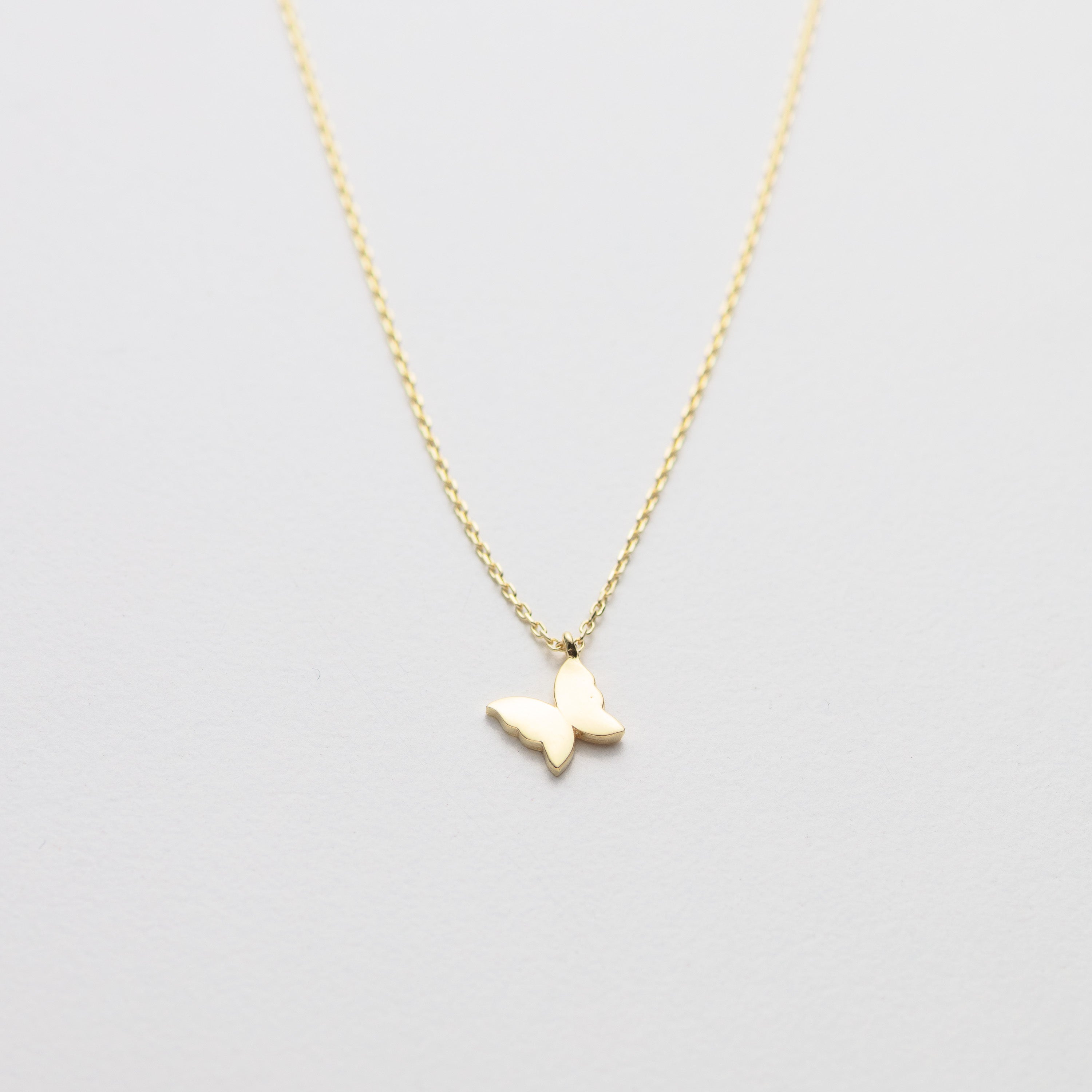 Gold butterfly necklace on a light gray background