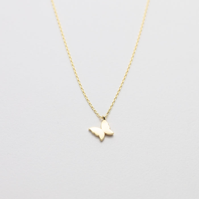 Gold butterfly necklace on a light gray background