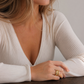 Woman wearing a white ribbed sweater with a deep neckline, sitting at a wooden table.