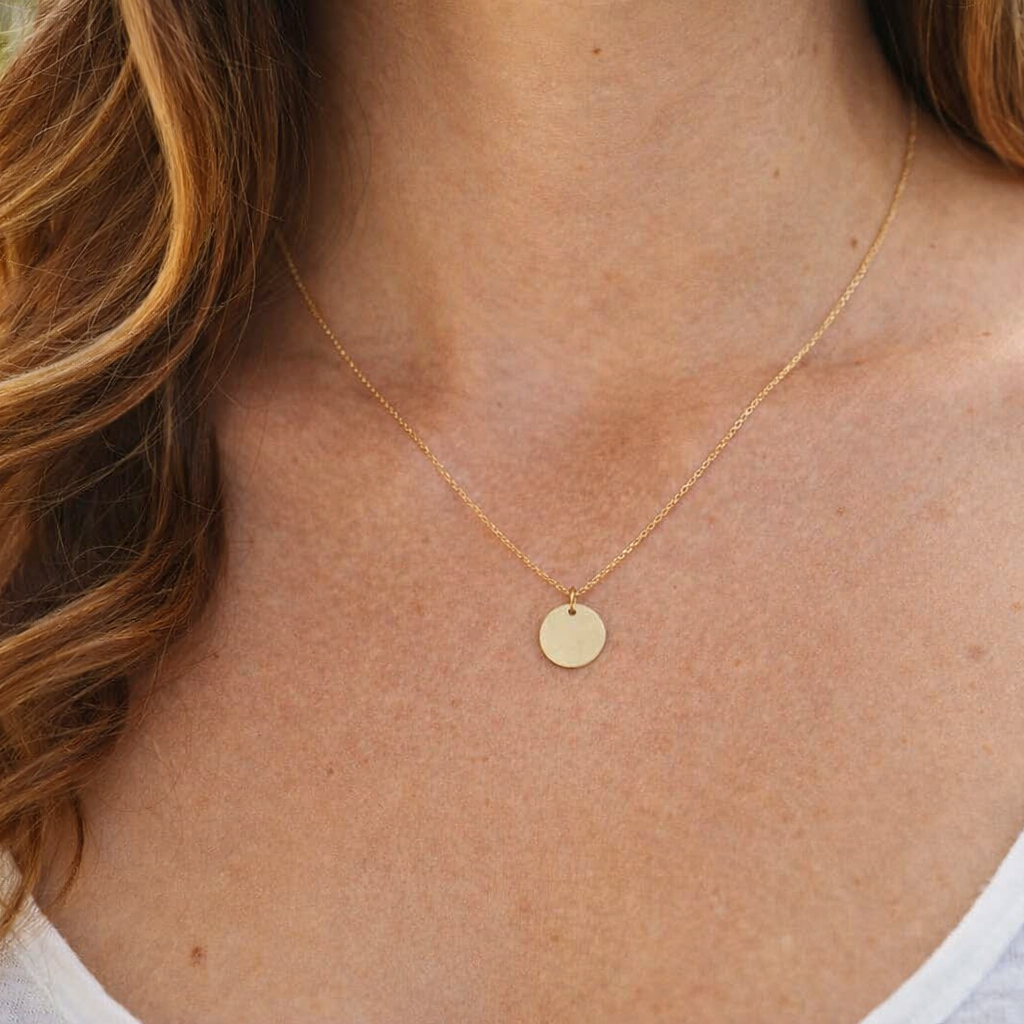 Gold necklace with a round pendant worn by a person with wavy hair.