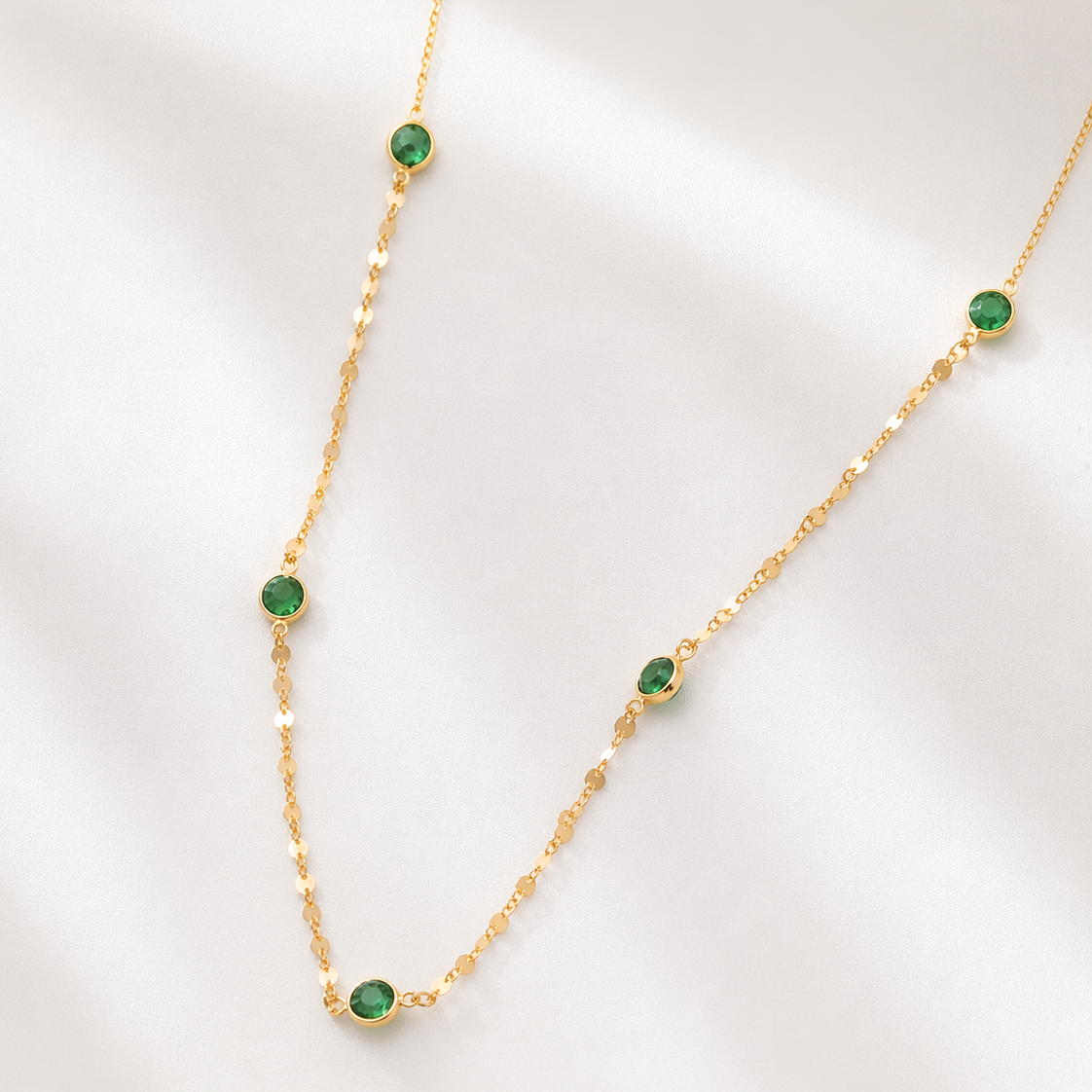 Gold necklace with green gemstones on a light gray background