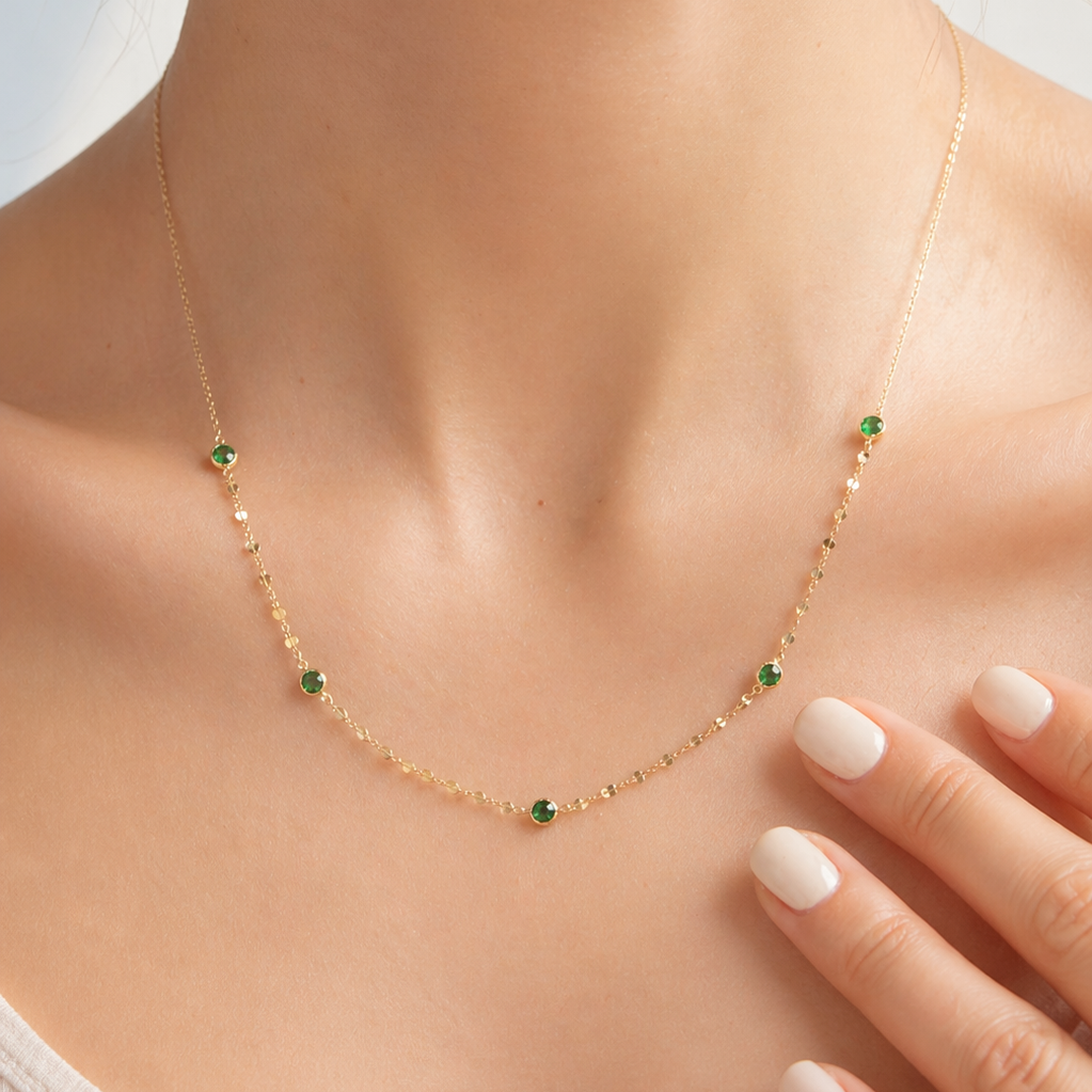 Necklace with green gemstones on a mannequin neck, with a hand touching the necklace.