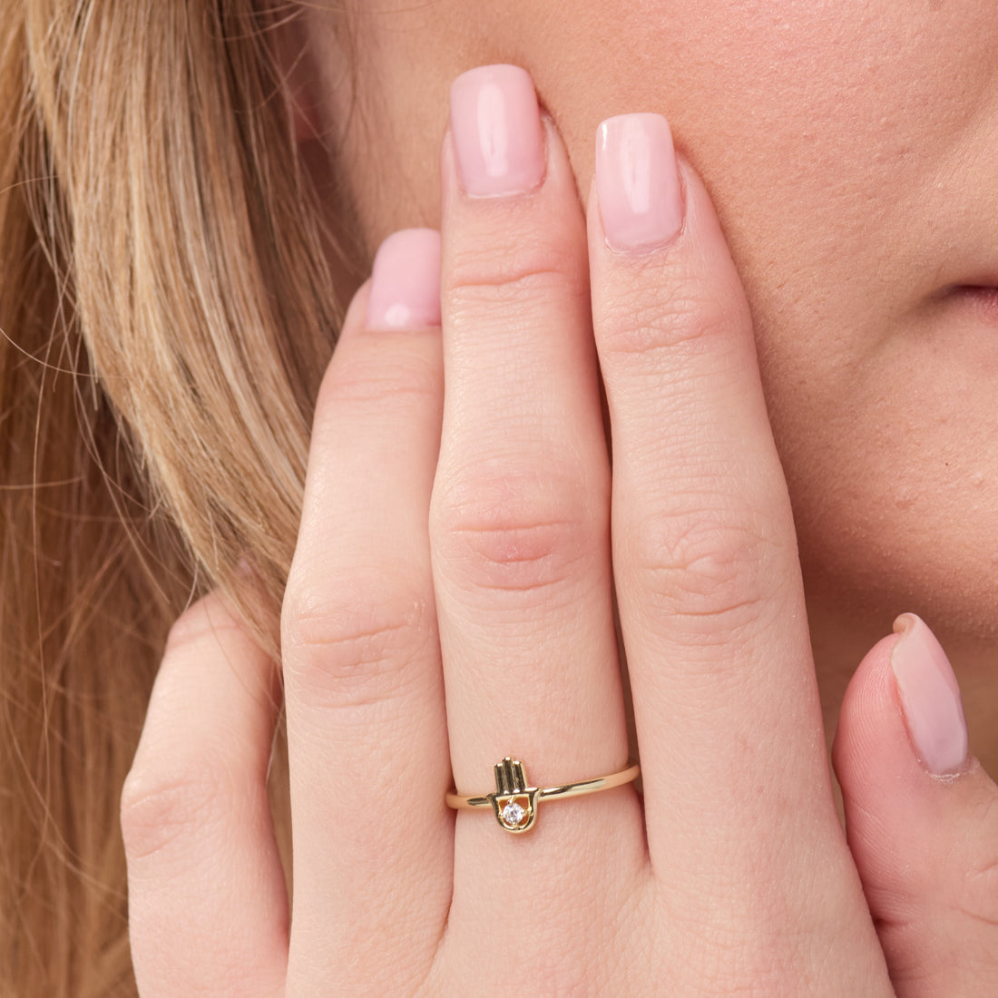 Gold ring with a small design on a person's finger against a neutral background