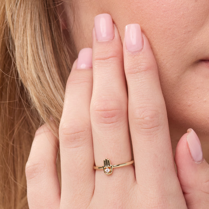 Gold ring with a small design on a person's finger against a neutral background