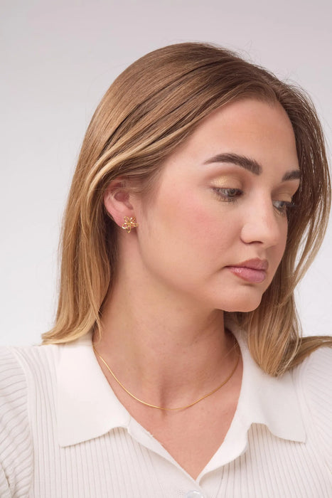 Woman wearing gold earrings and a necklace against a white background