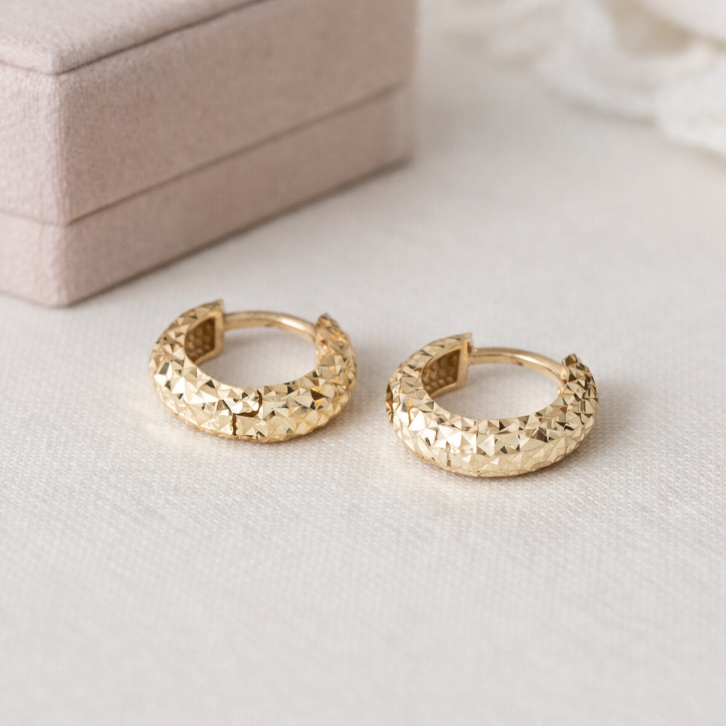Gold hoop earrings on a light surface with a jewelry box in the background