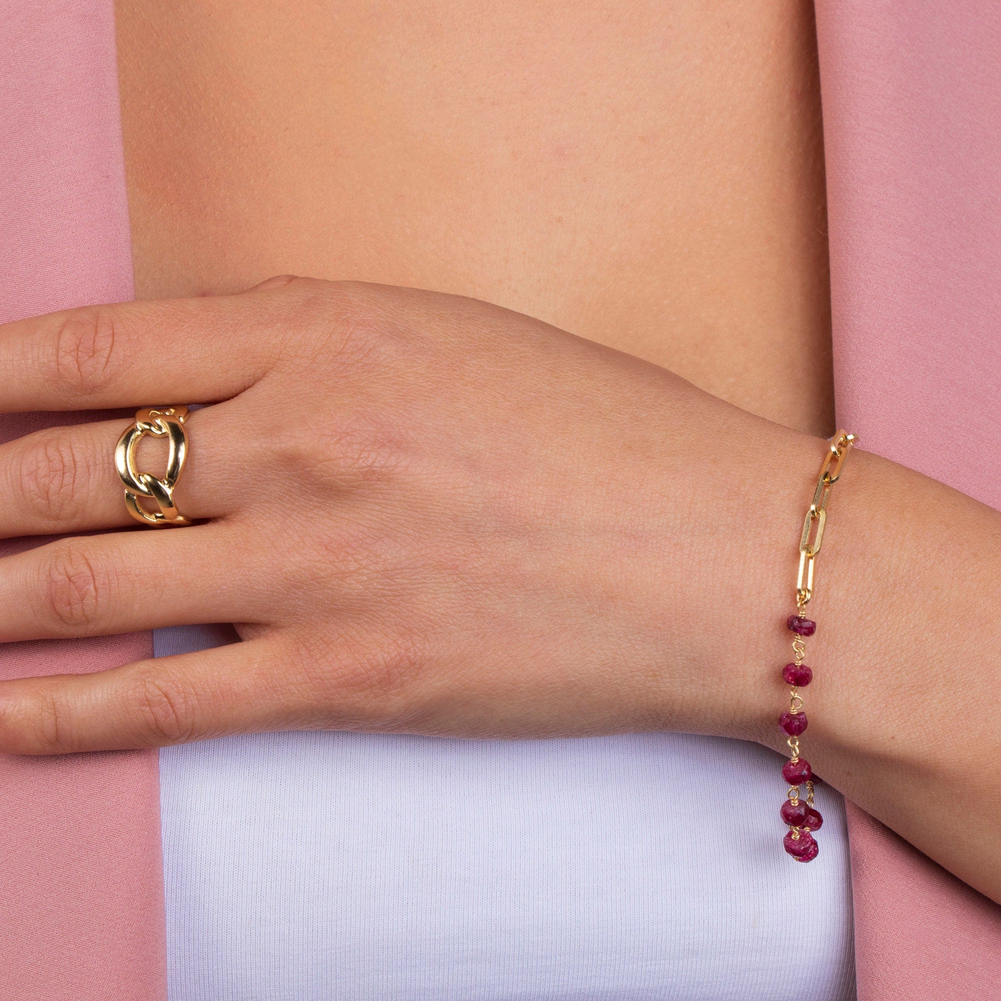 Hand wearing a gold ring and bracelet on a pink and white striped background