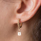 Gold hoop earring with a lock charm worn by a person