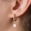 Gold hoop earring with a lock charm worn by a person