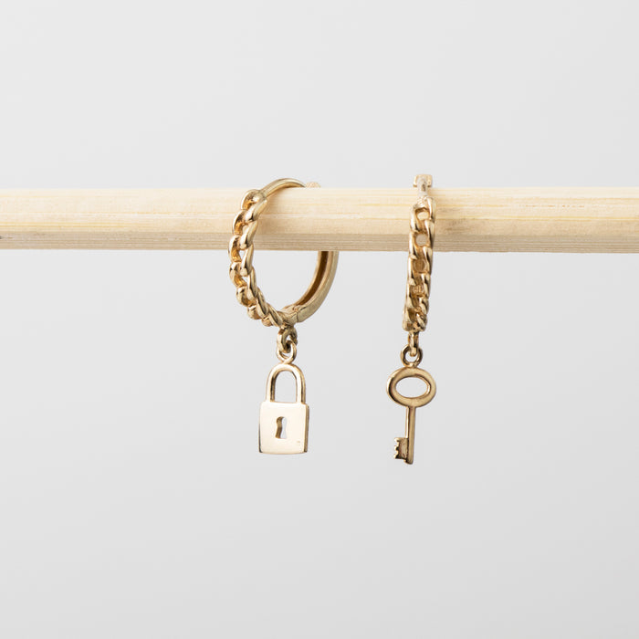 Gold chain bracelet with lock and key charms on a light gray background
