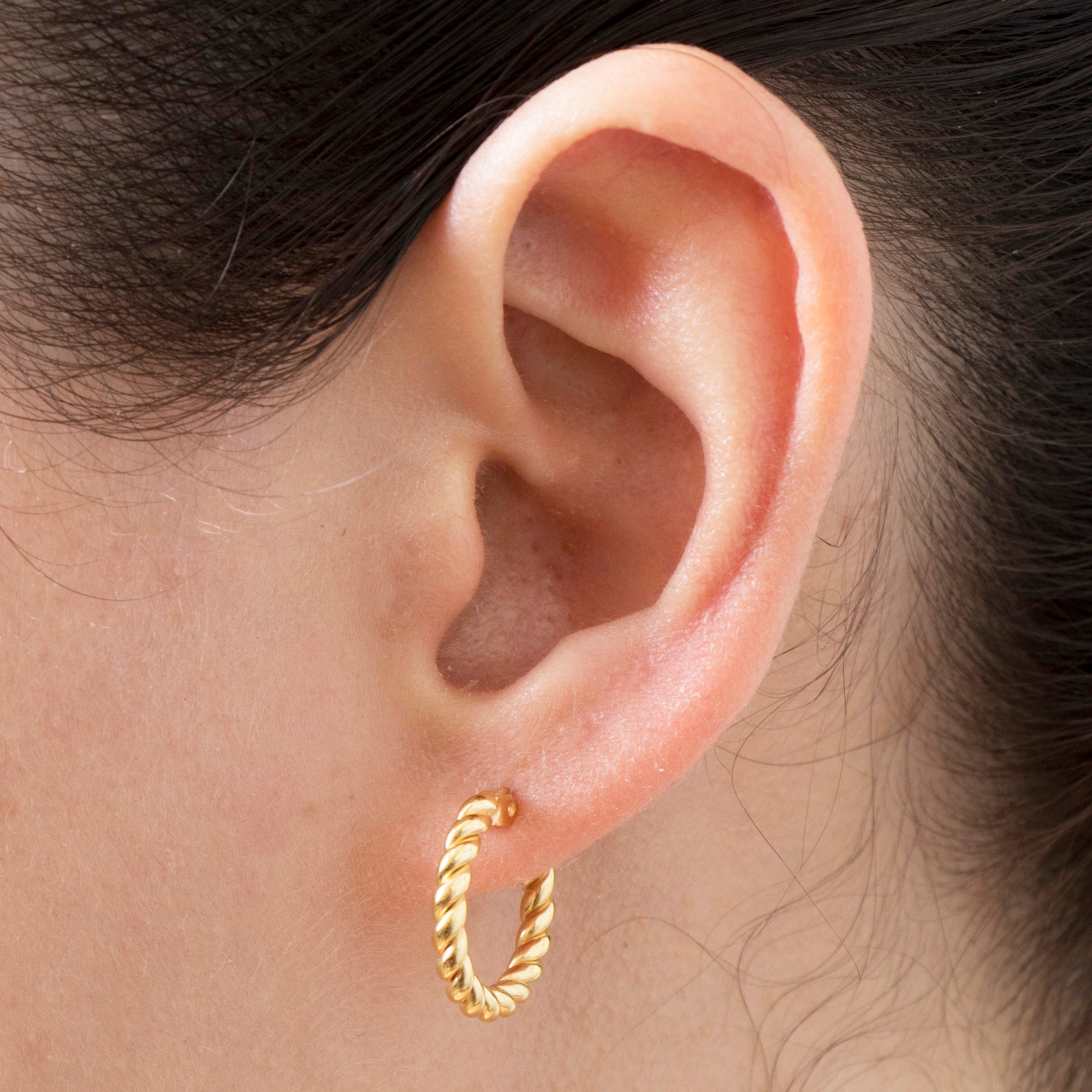 Gold hoop earring worn on an ear with a neutral background