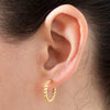 Gold hoop earring worn on an ear with a neutral background