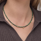 Green beaded necklace with gold accents worn by a person in a brown ribbed sweater.
