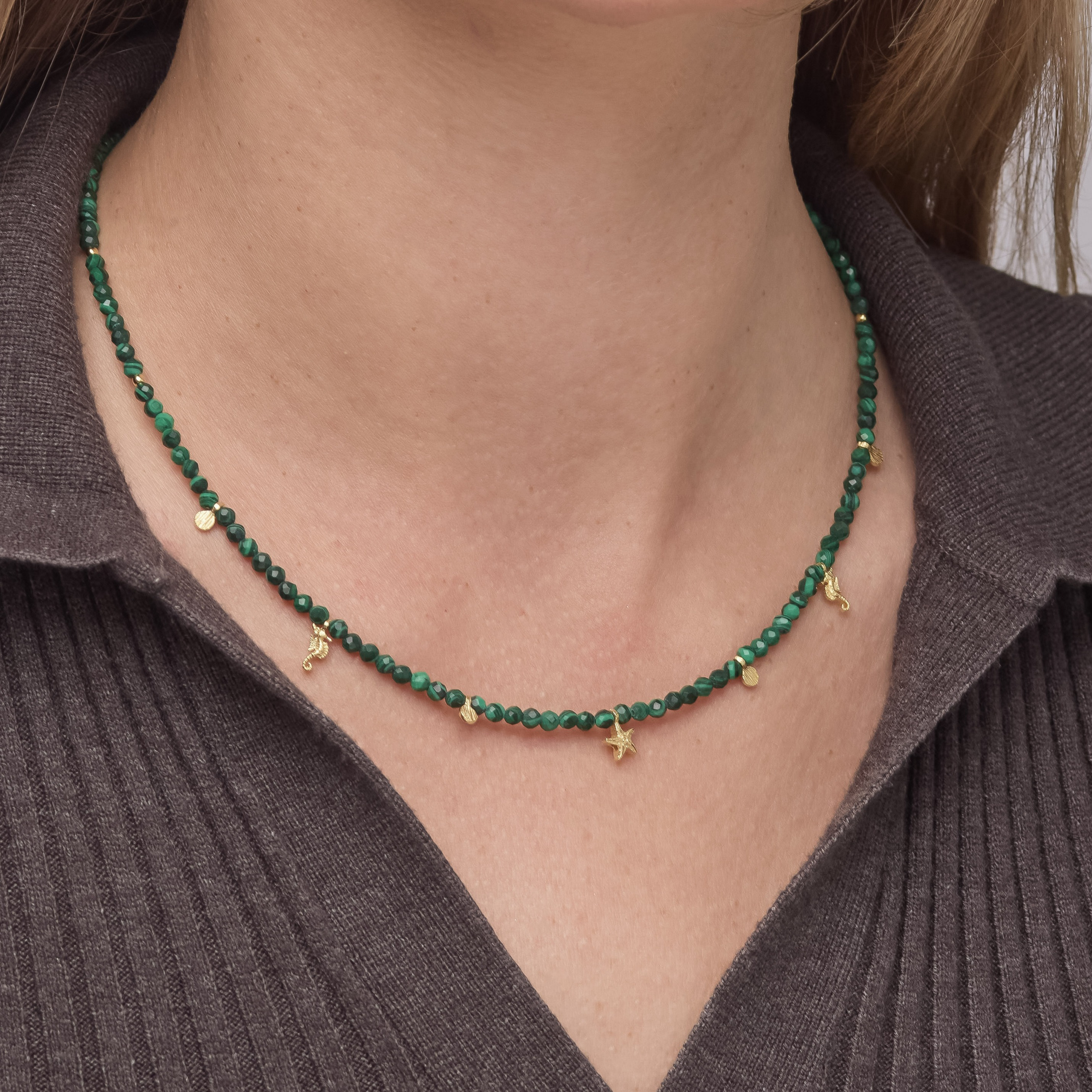 Green beaded necklace with gold accents worn by a person in a brown ribbed sweater.