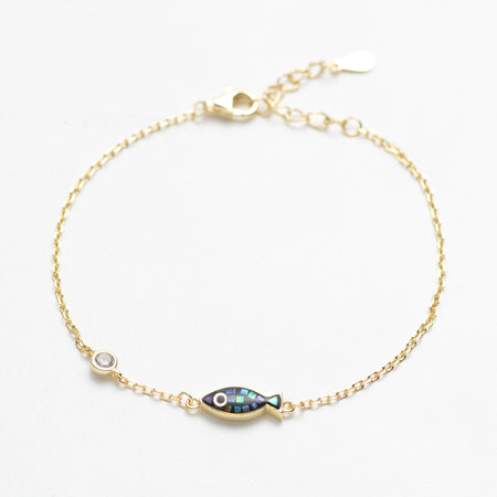 Gold bracelet with a fish-shaped charm on a white background