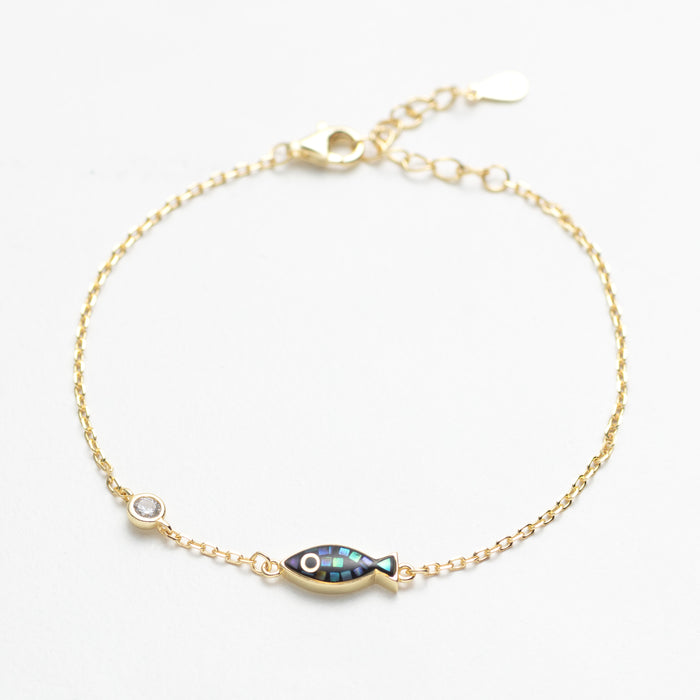 Gold bracelet with a fish-shaped charm on a white background