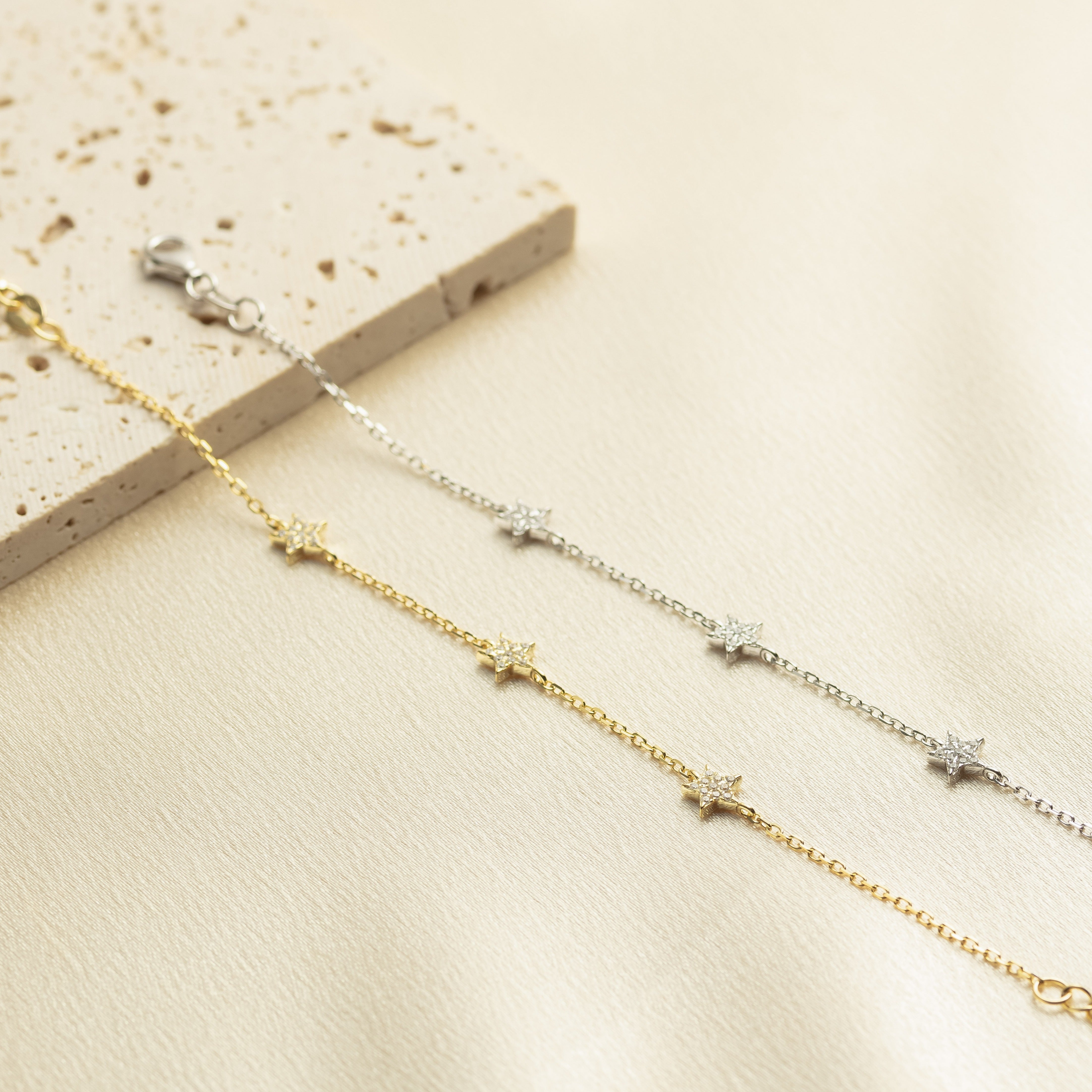 Two gold necklaces with star-shaped pendants on a beige surface