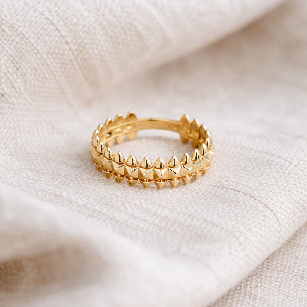 Gold ring with pyramid design on a beige fabric background